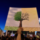Person holding a drawing of a tree, half with green leaves, half dead and dry.